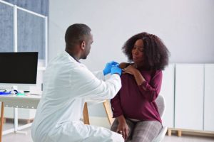 Male doctor wearing protective gloves administering a vaccine injection to the arm of a female patient in a modern medical clinic