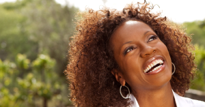 HPV vaccine: Close-up of a smiling Black woman with curly hair looking up towards the sky, wearing hoop earrings.